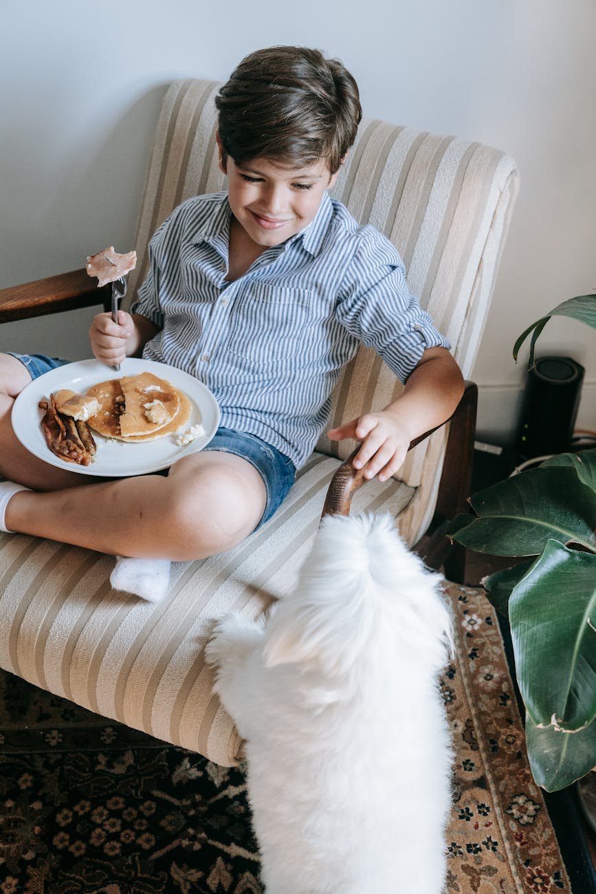 a boy playing with his dog while eating breakfast